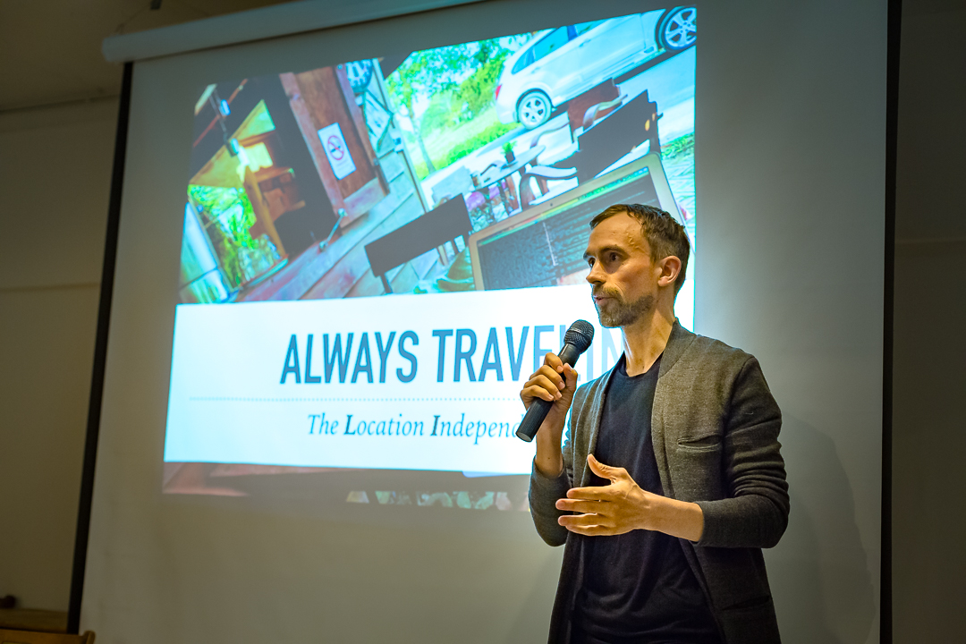 Chris Kirkland speaking with a microphone at Travel Massive Tokyo, in front of a slide reading Always Travelling: The Location Independent Lifestyle